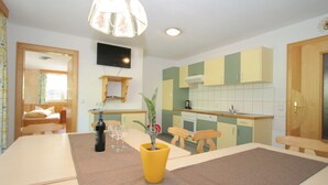 Een kleine keuken met een eethoek, een aan de muur bevestigde televisie en een houten deur.