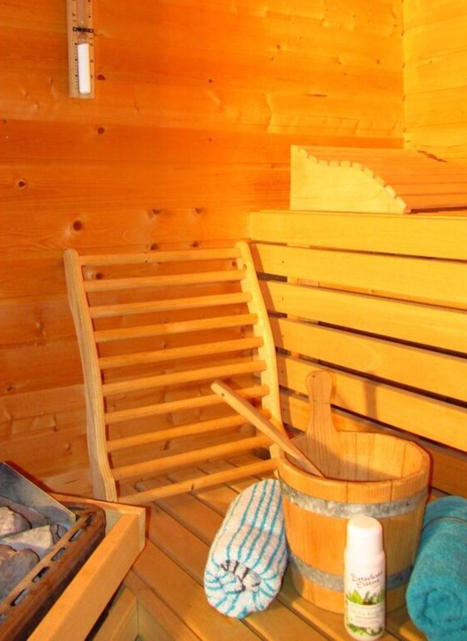 A wooden sauna with a slatted wooden bench, a wooden bucket, a towel, and a bottle of bath salts.