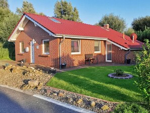 Une maison de plain-pied en briques, avec un toit rouge, un petit porche et une pelouse bien entretenue.
