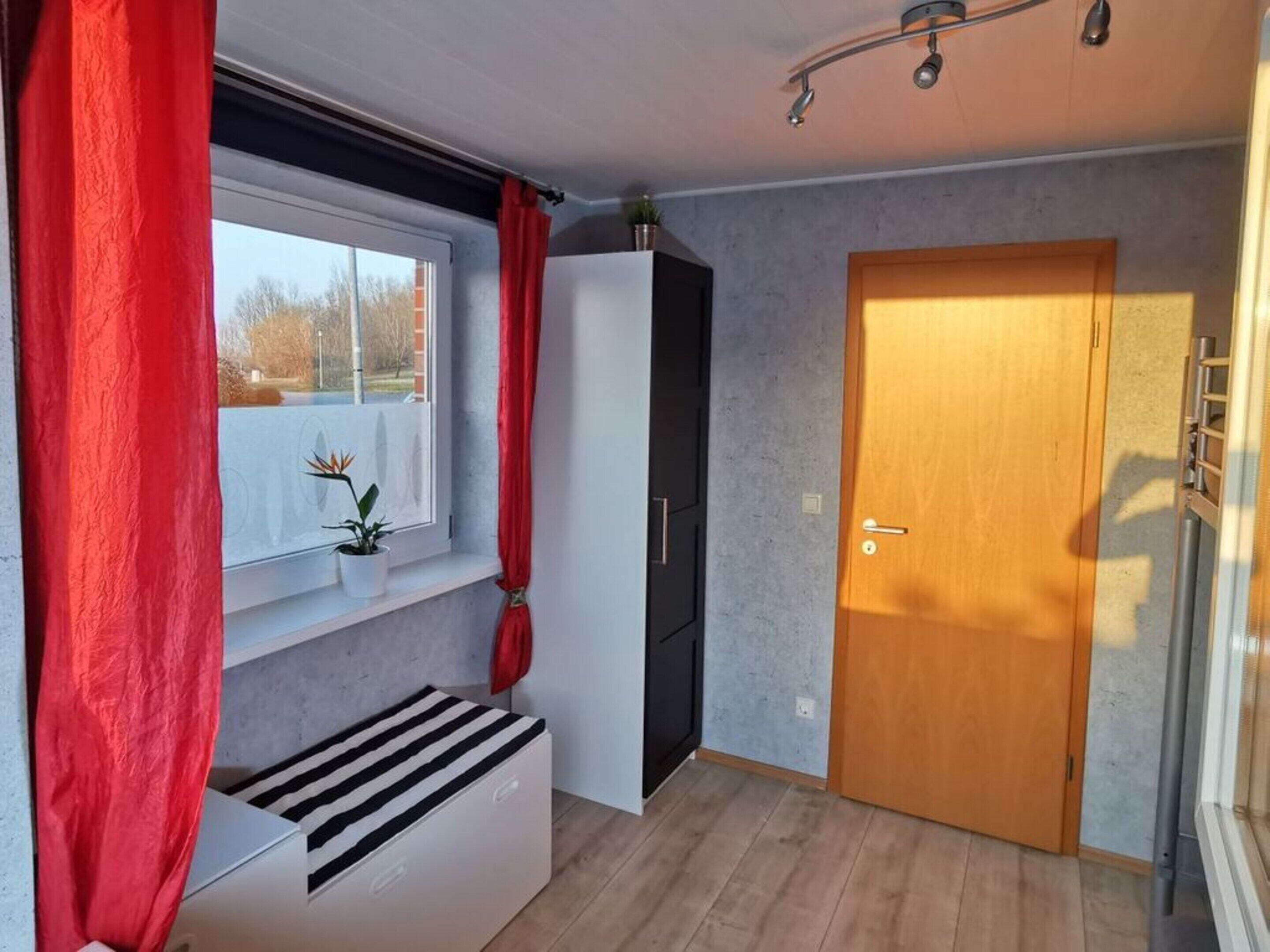 Ein Zimmer mit Fenster, Holztür und weißem Schrank.