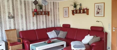 A living room with a red sofa, a wooden coffee table, a wicker chair, and a floor lamp.