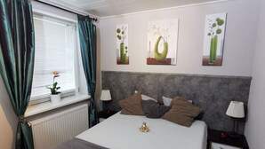 A neatly arranged bedroom with a bed, bedside tables, a window with curtains, and wall art. - Holiday Home Coastal Star (Otterndorf)