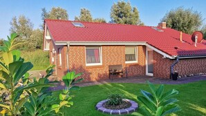 A single-story brick house with a red tiled roof, a small patio with a bench, and a well-maintained lawn. - Holiday Home Coastal Star (Otterndorf)