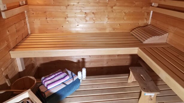 A sauna room with wooden benches, a bench for sitting, and a small bucket. - Holiday Home Coastal Star (Otterndorf)
