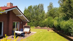 A brick house with a red roof, a small patio with a table and chairs, and a well-maintained lawn. - Holiday Home Coastal Star (Otterndorf)