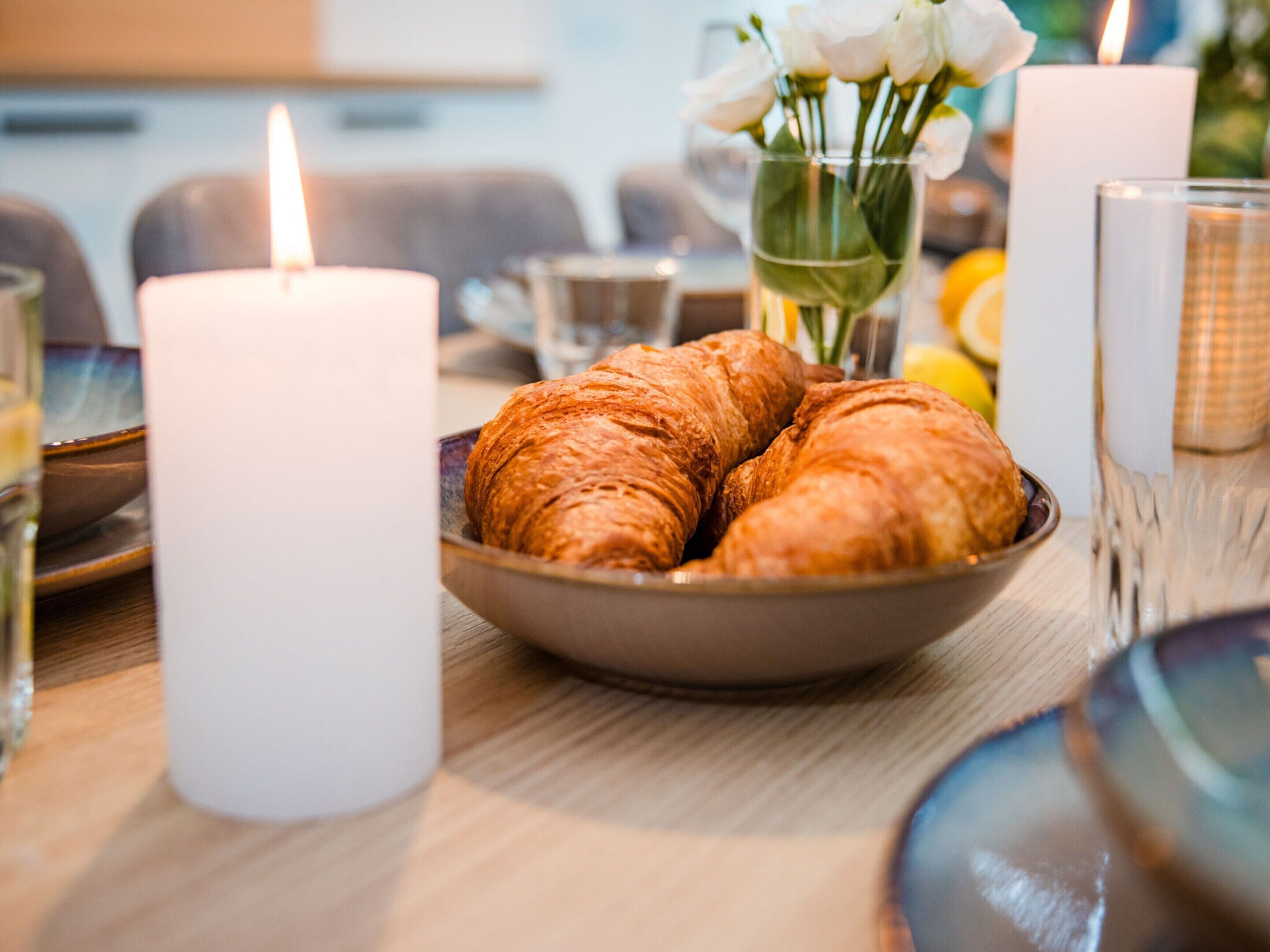 Une table avec un panier de croissants et une bougie allumée.