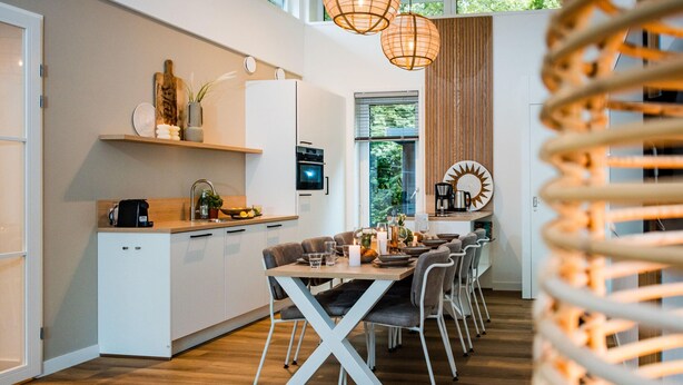Une cuisine moderne avec des meubles blancs, un coin repas doté d’une table et de chaises en bois, et une grande fenêtre qui laisse entrer la lumière naturelle.