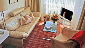 Una sala de estar con un sofá color beige, una mesita de centro, un televisor y una ventana con cortinas.