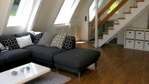 Een moderne loft-achtige woonruimte met een donkergrijze hoekbank, een witte salontafel en een trap met houten leuningen.