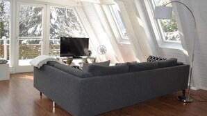 Een moderne woonkamer met een grijze hoekbank, een flatscreen televisie en een vloerlamp.
