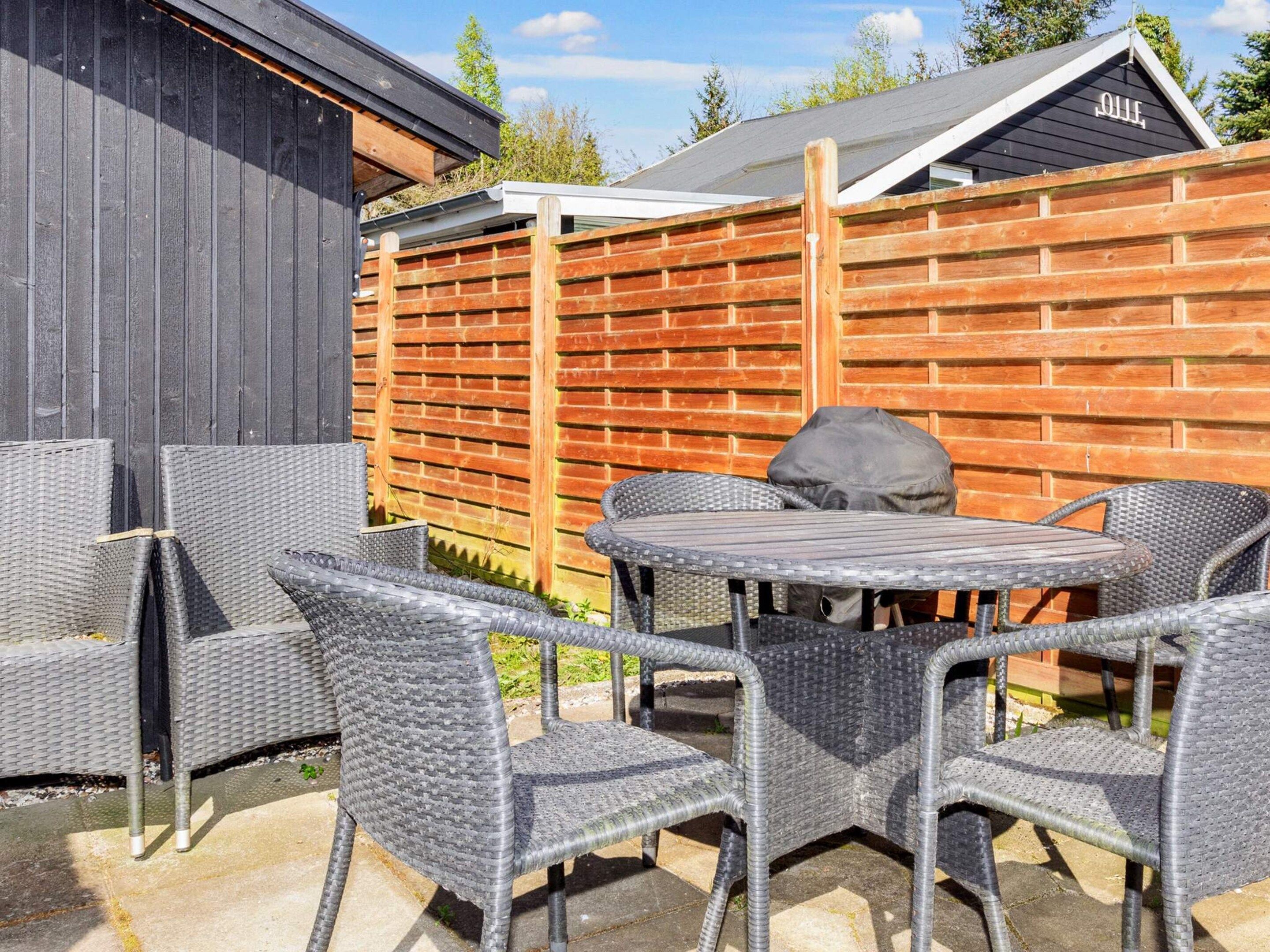 An outdoor seating area with wicker chairs and a round table, enclosed by a wooden fence.