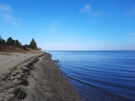 En strand med gruset bund, roligt vand og en klar himmel.