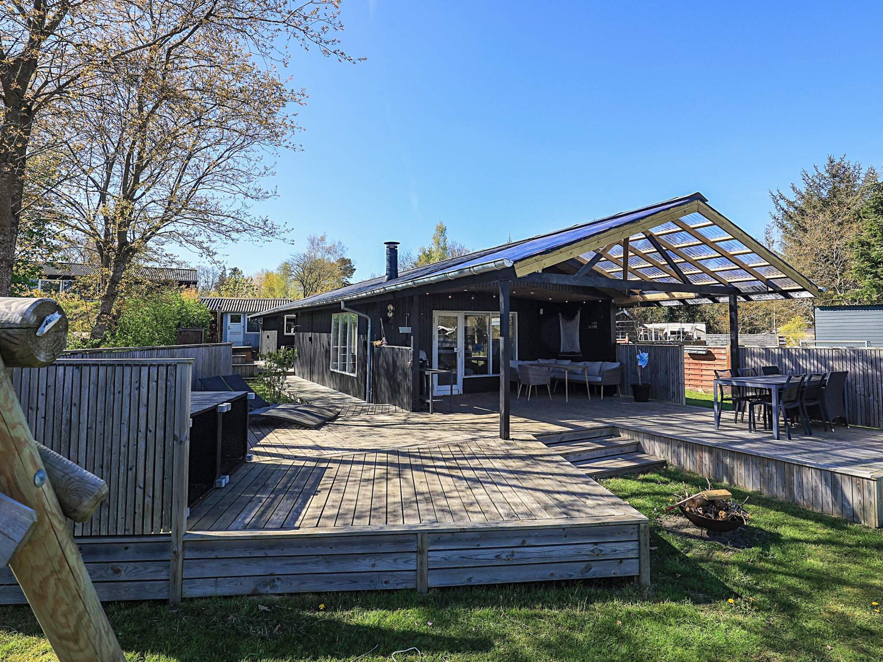 Eine Holzterrasse mit überdachtem Patio, Sitzgelegenheiten im Freien und einem Grill.
