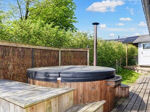 A hot tub with a wooden deck and a bamboo fence in a backyard. - 6 Person Holiday Home in Hojslev (Hojslev)