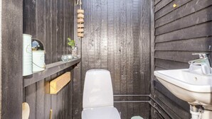 A compact bathroom with a white toilet, a sink, and a wooden shelf with decorative items. - 6 Person Holiday Home in Hojslev (Hojslev)