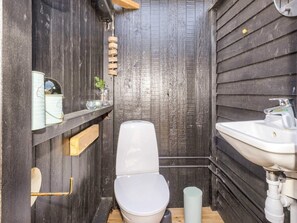 A compact bathroom with a white toilet, a sink, and a wooden shelf with decorative items. - 6 Person Holiday Home in Hojslev (Hojslev)