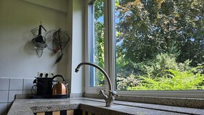 Une cuisine avec un dosseret à carreaux, une bouilloire en cuivre et une fenêtre donnant sur un paysage verdoyant.