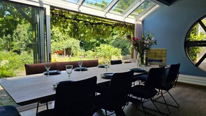 Un coin repas avec une table dressée pour quatre personnes, de grandes fenêtres et une vue sur la verdure environnante.