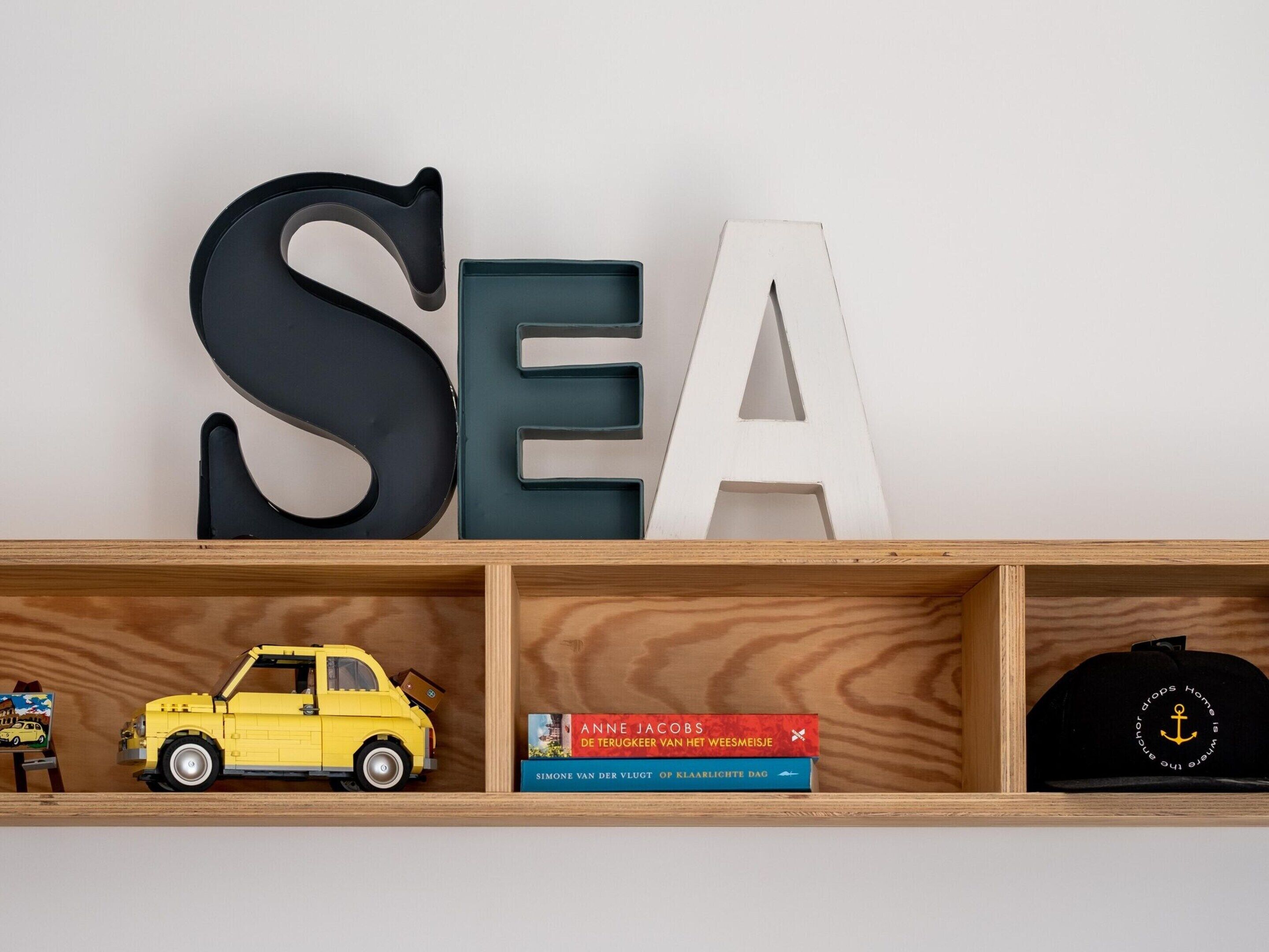 A shelf with large letters spelling "SEA," a yellow toy car, two books, and a black cap.