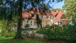 A large, yellow building with a red-tiled roof, surrounded by lush greenery and trees. - Ferienhaus mit Garten, Eschede (Eschede)