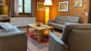 A cozy cabin interior with a wooden interior, a sofa, a table with a bowl of fruit, and a radiator. - Ferienhaus mit Garten, Eschede (Eschede)