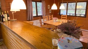 A wooden cabin interior with a dining table, chairs, a bar area with bottles, and hanging pendant lights. - Ferienhaus mit Garten, Eschede (Eschede)