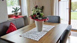 Un'area pranzo con tavolo in legno, un vaso di fiori e vista sull'esterno.