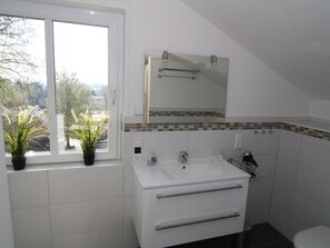 A bathroom with a white sink, a mirror above it, and a window with plants. - Schittering van de Zee (Sellin)