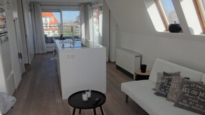A modern apartment with a kitchen, dining area, and living room. It features large windows, a white sofa, and a small black table. - Apartment in Nieuwpoort With Terrace (Nieuwpoort)