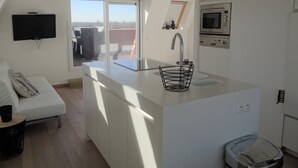 A modern kitchen with a large island, a built-in oven, and a wall-mounted TV. - Apartment in Nieuwpoort With Terrace (Nieuwpoort)