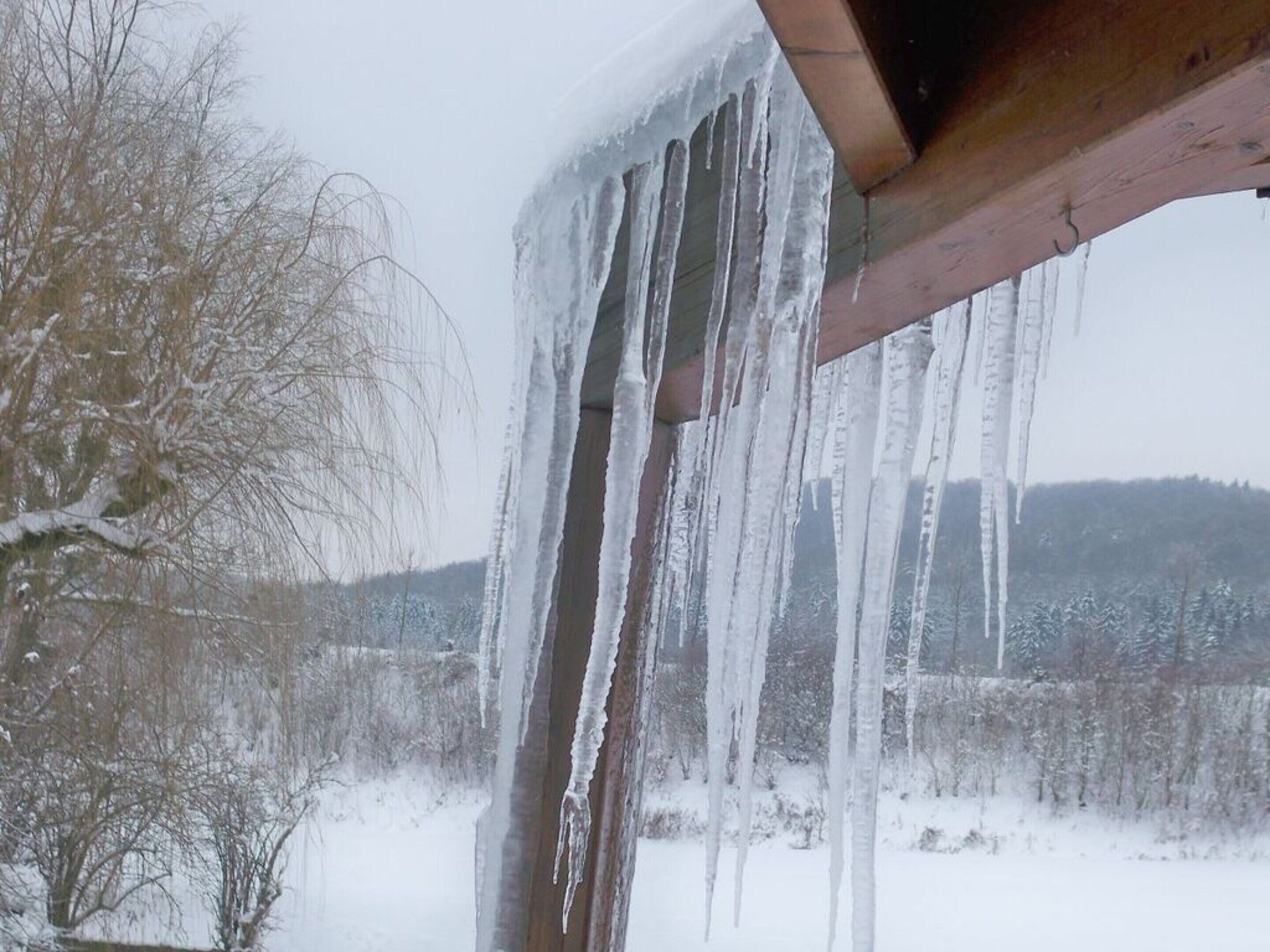 Eiszapfen hängen an einer Holzhütte in einer verschneiten Landschaft.