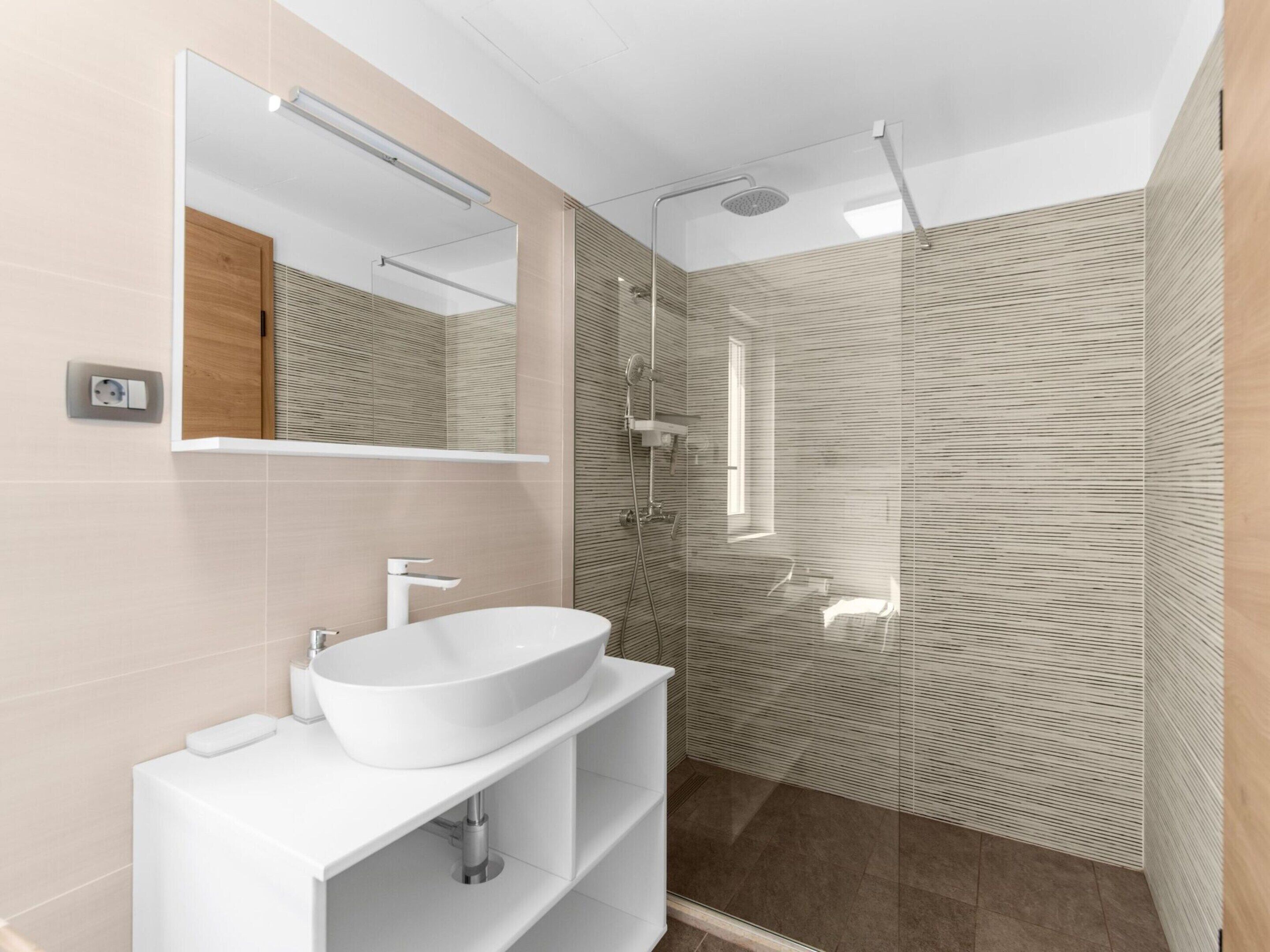 A modern bathroom with a large mirror, a white sink, and a glass shower enclosure.