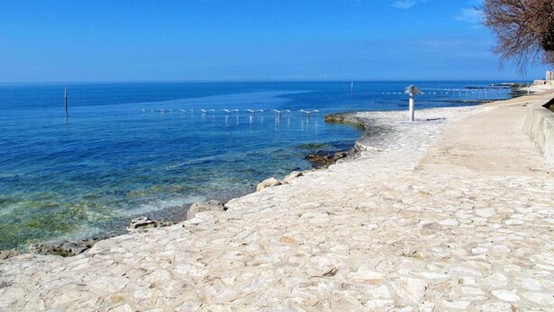 A coastal walkway with clear blue sea, stone pavement, and a distant pier. - Villa in Istria With Heated Eco Pool (Brtonigla)