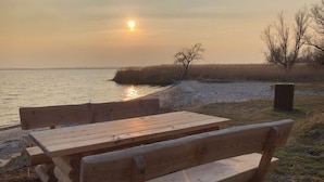 Une table et un banc en bois, installés au bord d’un lac, au coucher du soleil.