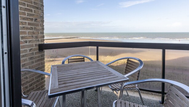 Un balcón con mesa y sillas con vista a la playa.