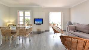 Una sala de estar moderna con comedor, un televisor de pantalla plana en la pared, mobiliario de mimbre y un sofá gris.