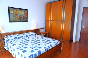 A bedroom with a bed, a chair, a wardrobe, and a painting on the wall.