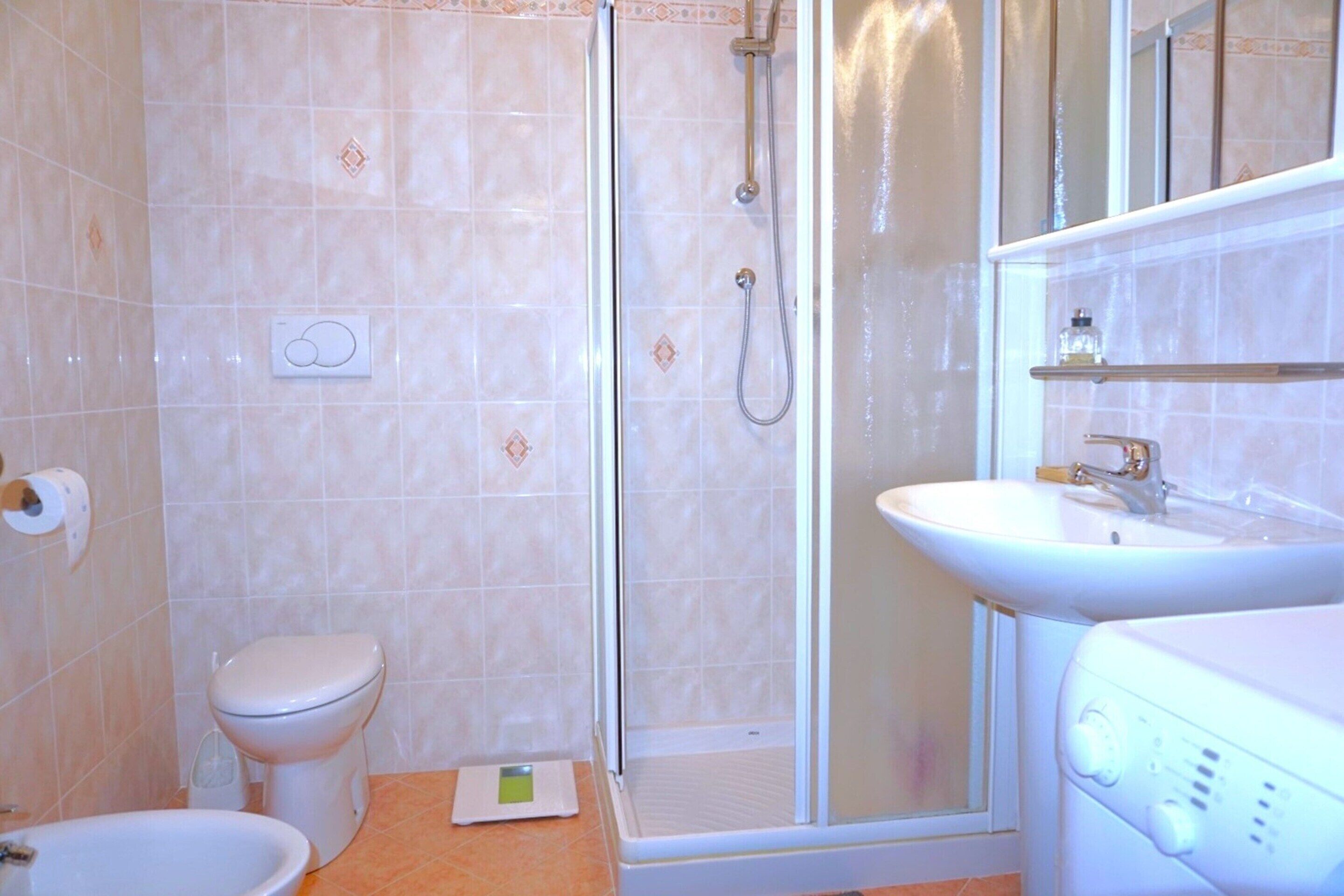 Een badkamer met toilet, douche, wastafel en een weegschaal op de vloer.