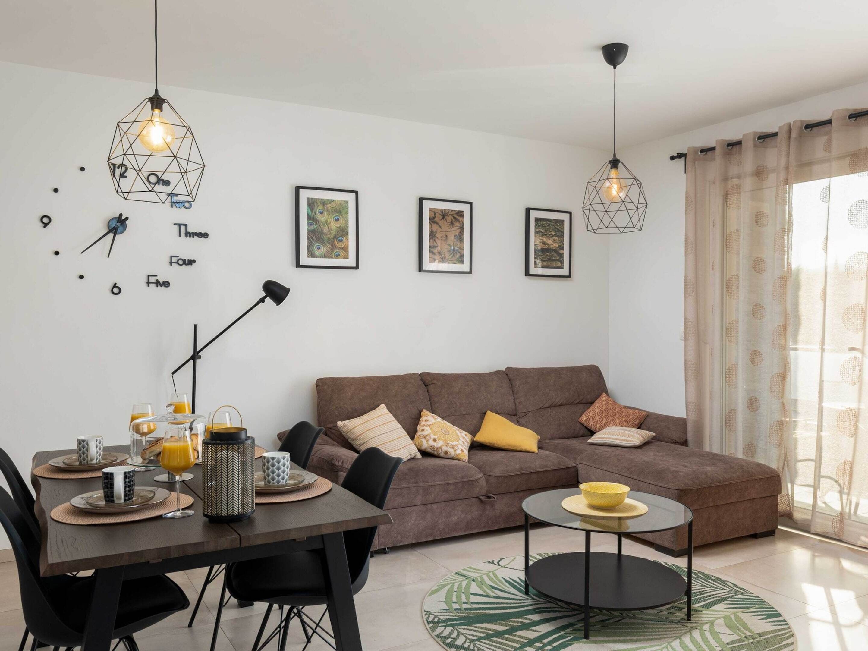 A modern living room with a brown sofa, a dining table with breakfast items, and geometric pendant lights.