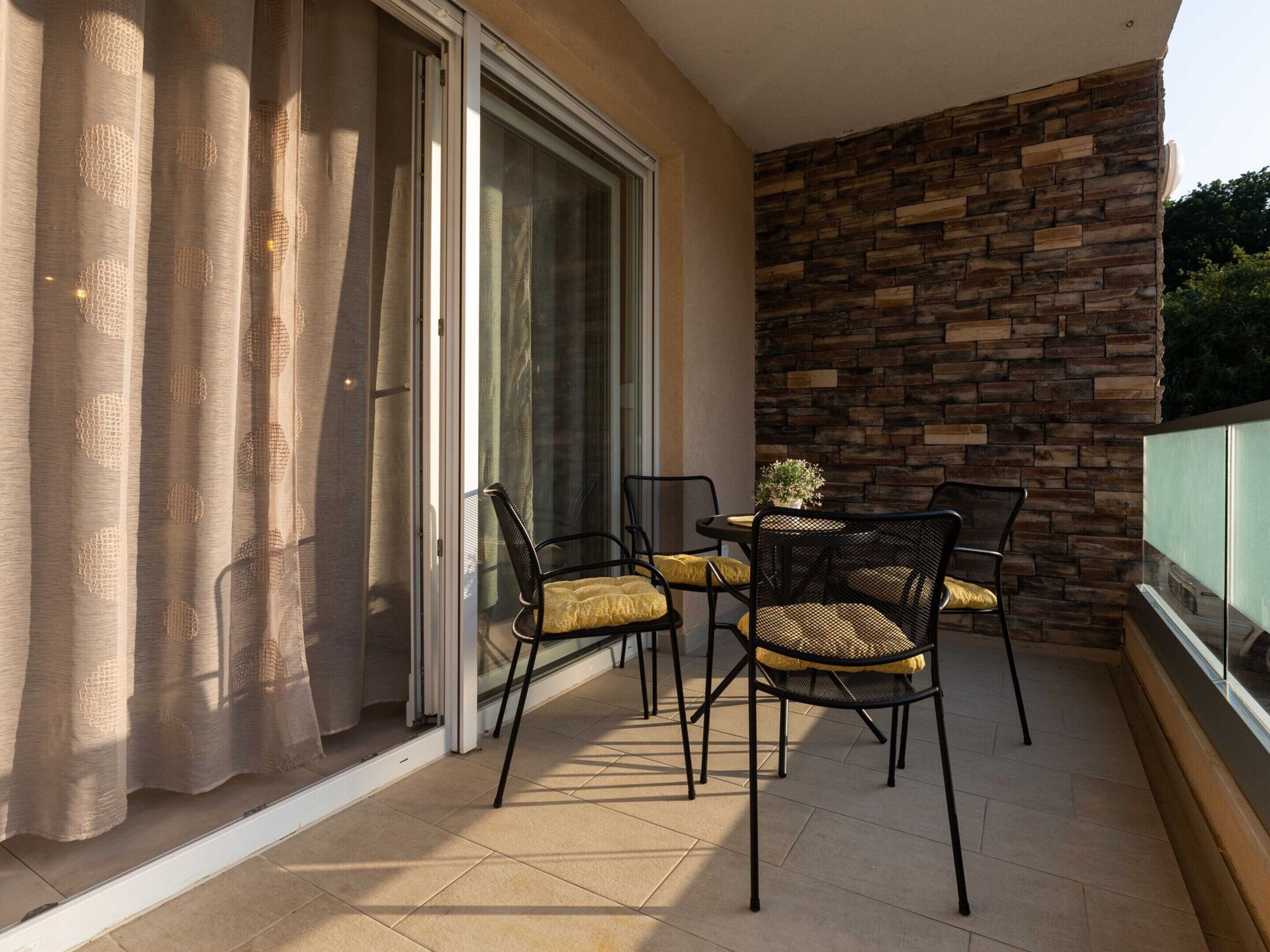 Un balcon avec un mur en pierre, une porte vitrée et une table avec des chaises.