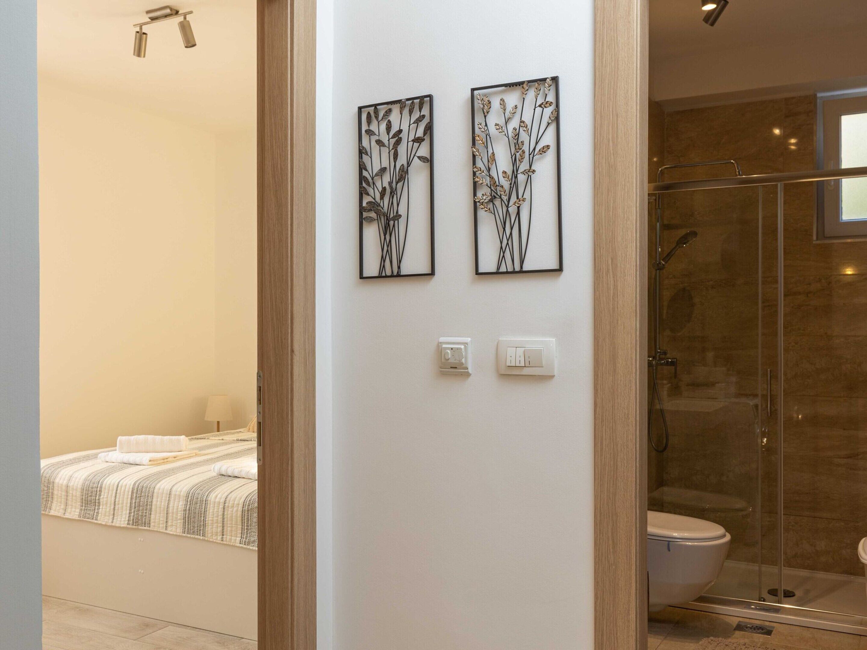 A modern bathroom with a glass shower enclosure, a toilet, and a bed with a striped bedspread.