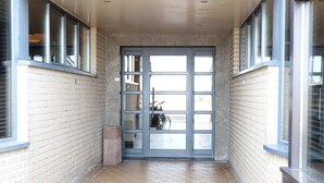 Un pasillo con suelo de baldosas, una puerta de cristal con marco metálico y ventanas a ambos lados.