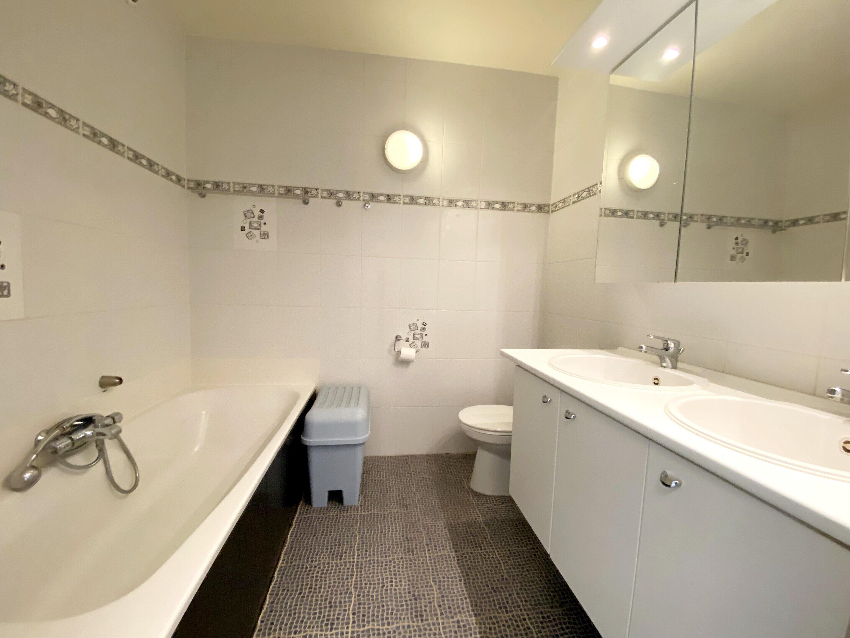 Un baño con bañera, dos lavamanos, inodoro y espejo.