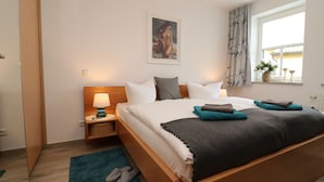 A neatly arranged hotel room with a large bed, a bedside table with a lamp, a window with curtains, and a framed picture on the wall.