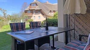 A patio with a table and chairs, a bottle of wine, and a view of a house with a balcony.
