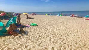 Una playa arenosa con sombrillas y toldos de colores, y gente relajándose.