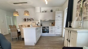 Una cocina moderna con armarios blancos, una isla central y un comedor con sillas de mimbre.