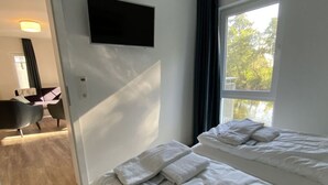 Habitación de hotel con dos camas, un televisor montado en la pared y vistas al exterior a través de una ventana.