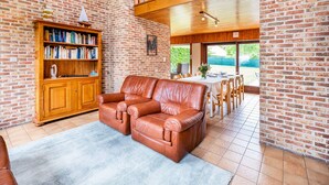 A spacious living room with a leather sofa, a wooden bookshelf, and a dining area with a table and chairs. - Villa in St-idesbald Near Sea Beach (Koksijde)