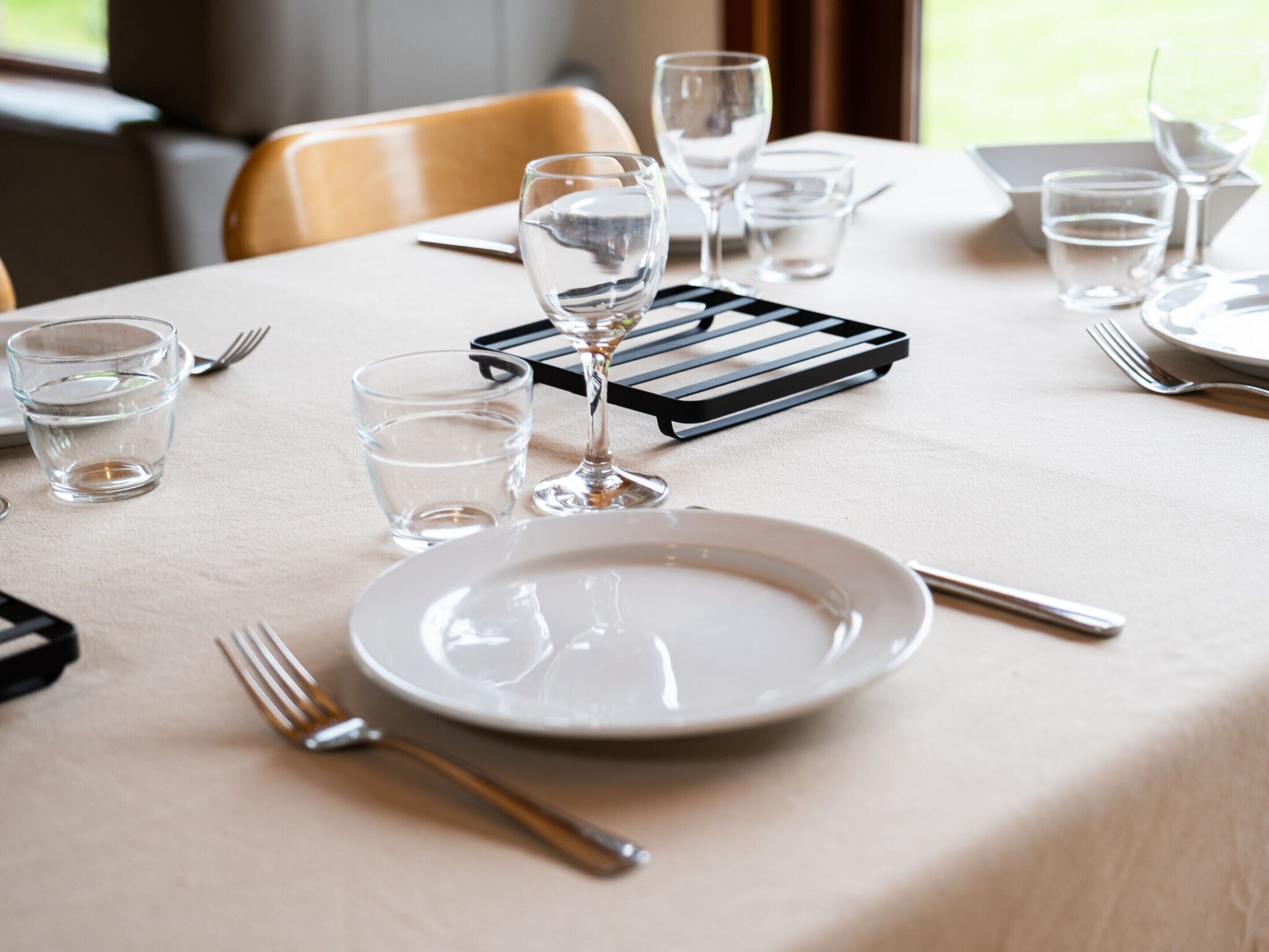 A table set with a white tablecloth, clear glasses, a wine glass, and cutlery.
